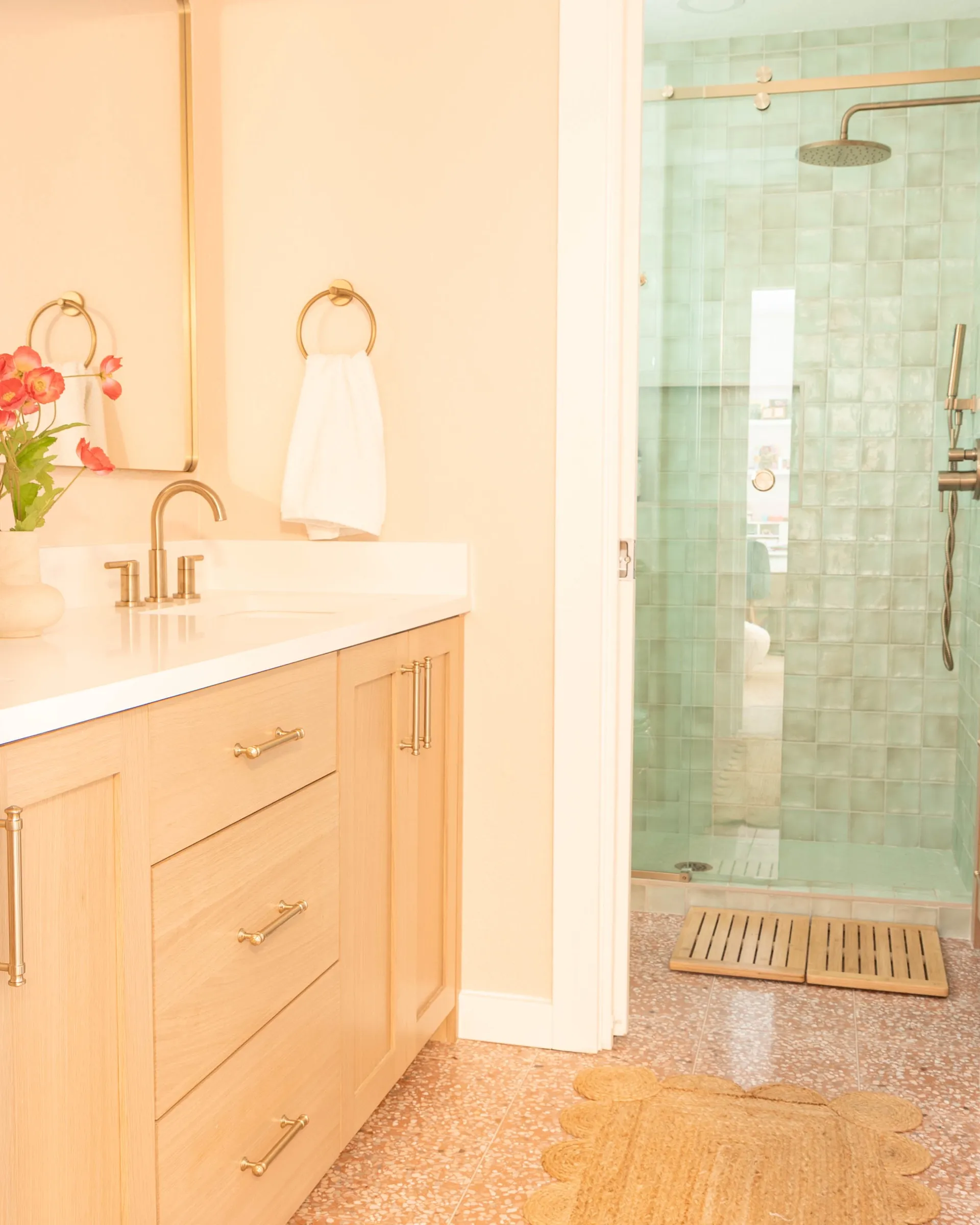 White oak vanity with brass fittings beside a walk-in shower lined in sea-green zellige tile