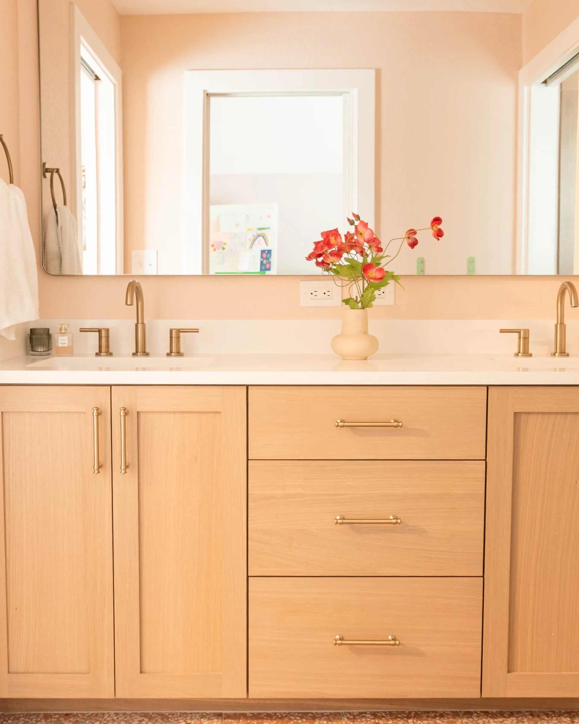 Long white oak vanity with a white stone counter and a vase of pink roses