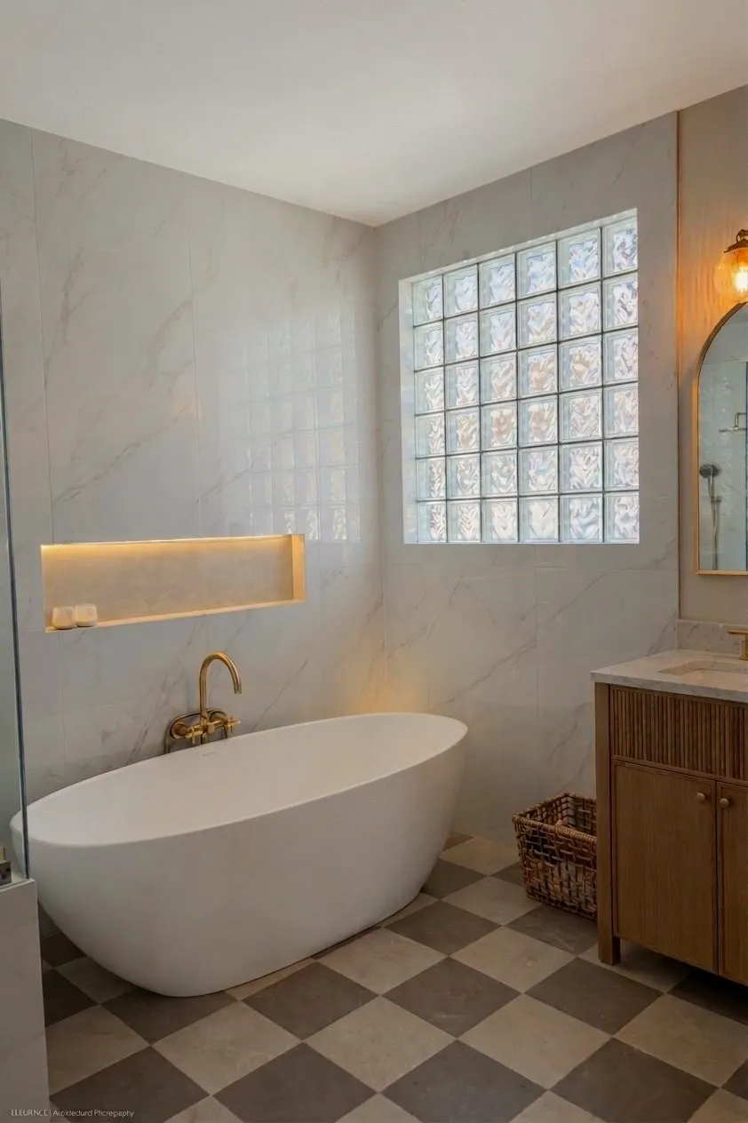 The bathroom in full: tub under the glass block window, lit niche along the wall and the checkerboard floor running to the vanity