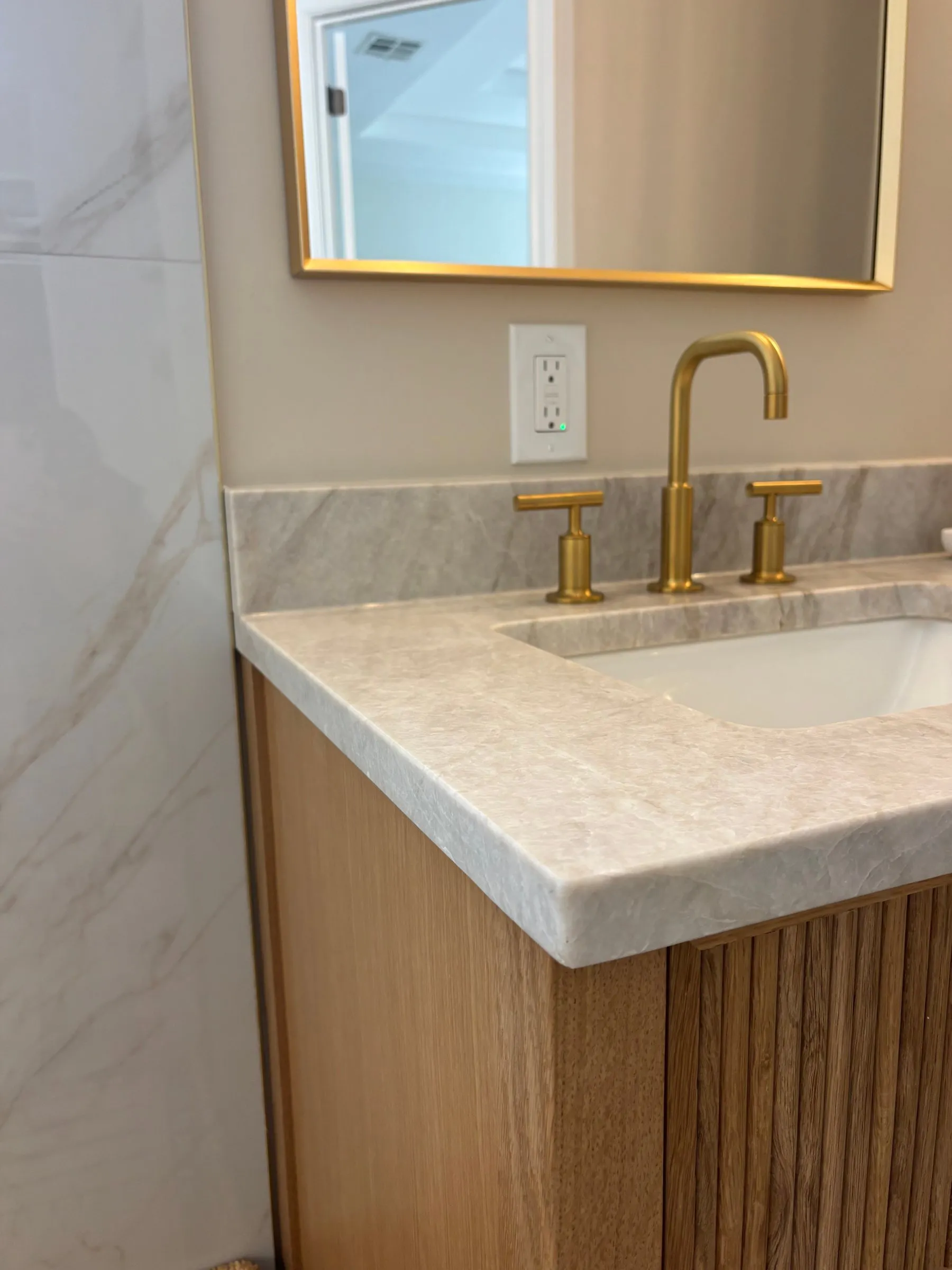 Brass tap set into the marble vanity top, fluted oak cabinetry below and a brass-framed mirror above