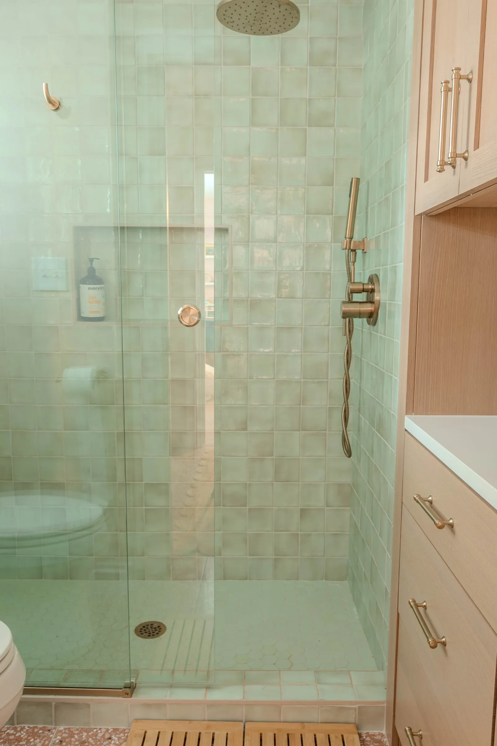 Glass shower enclosure tiled floor to ceiling in glossy sea-green zellige with an aged brass rainhead