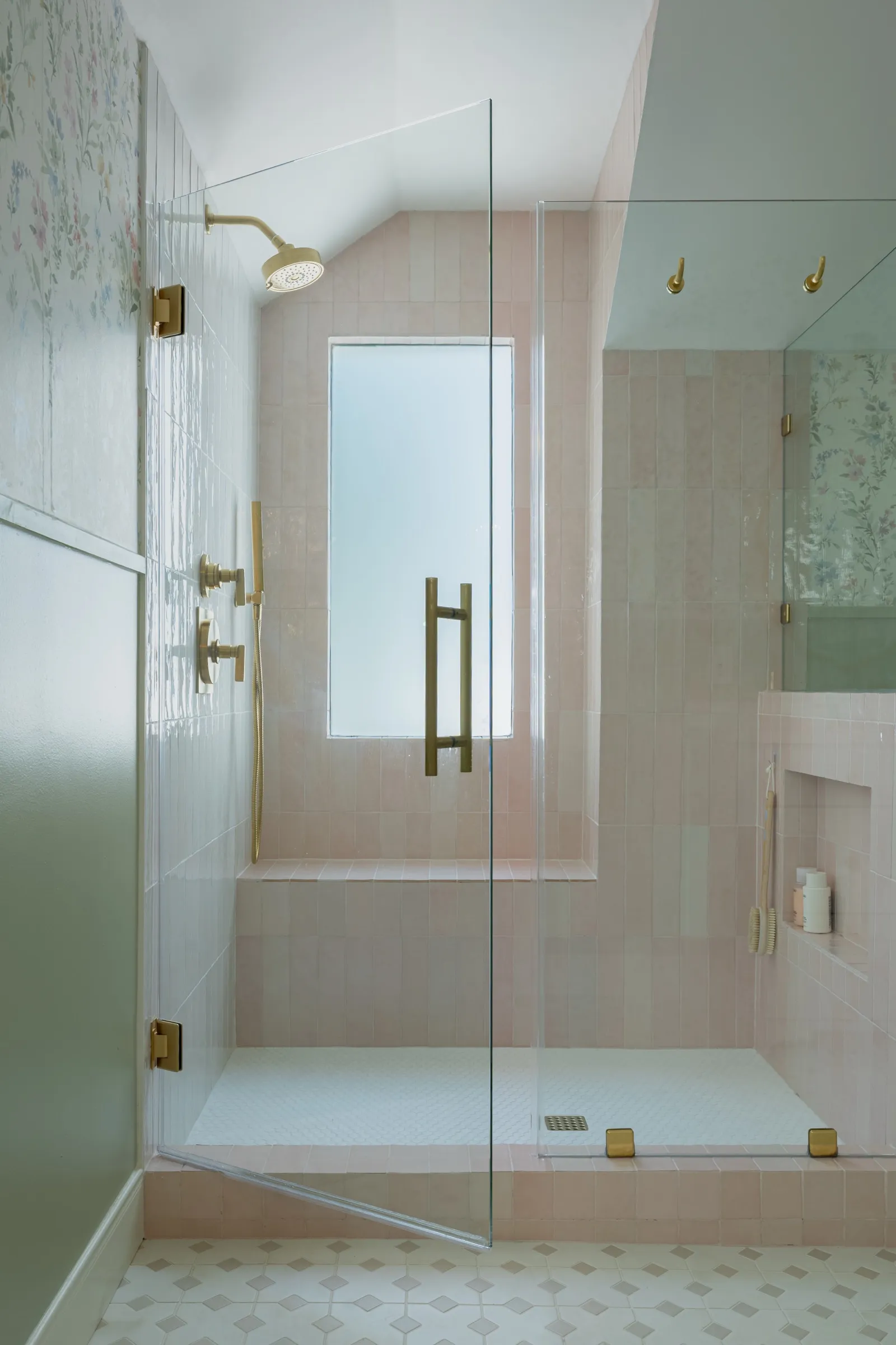 Inside the pink zellige shower, brass fittings and a frosted window under a sloping ceiling
