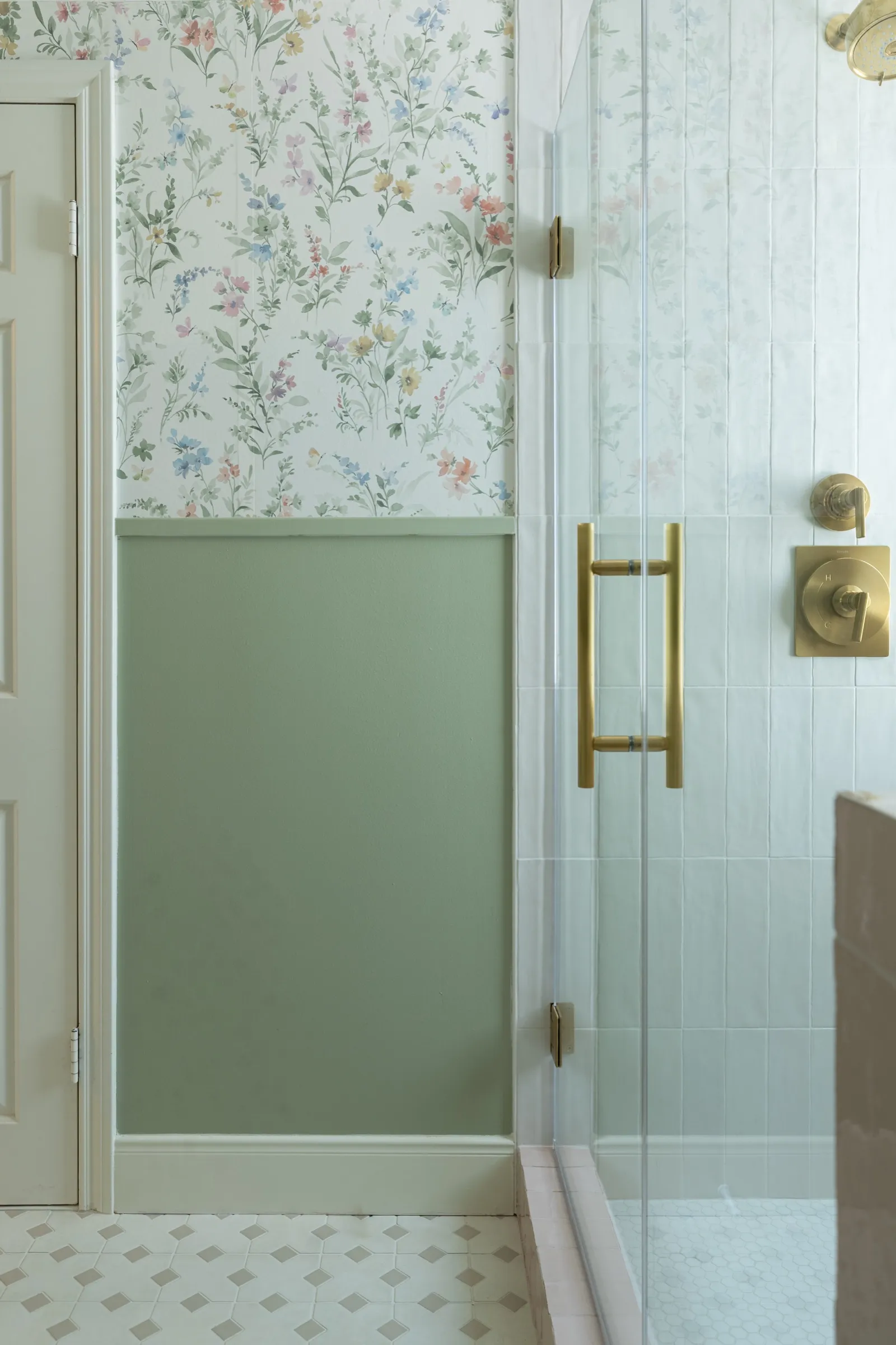 The shower seen from the doorway, brass handle against the glass with the papered wall alongside