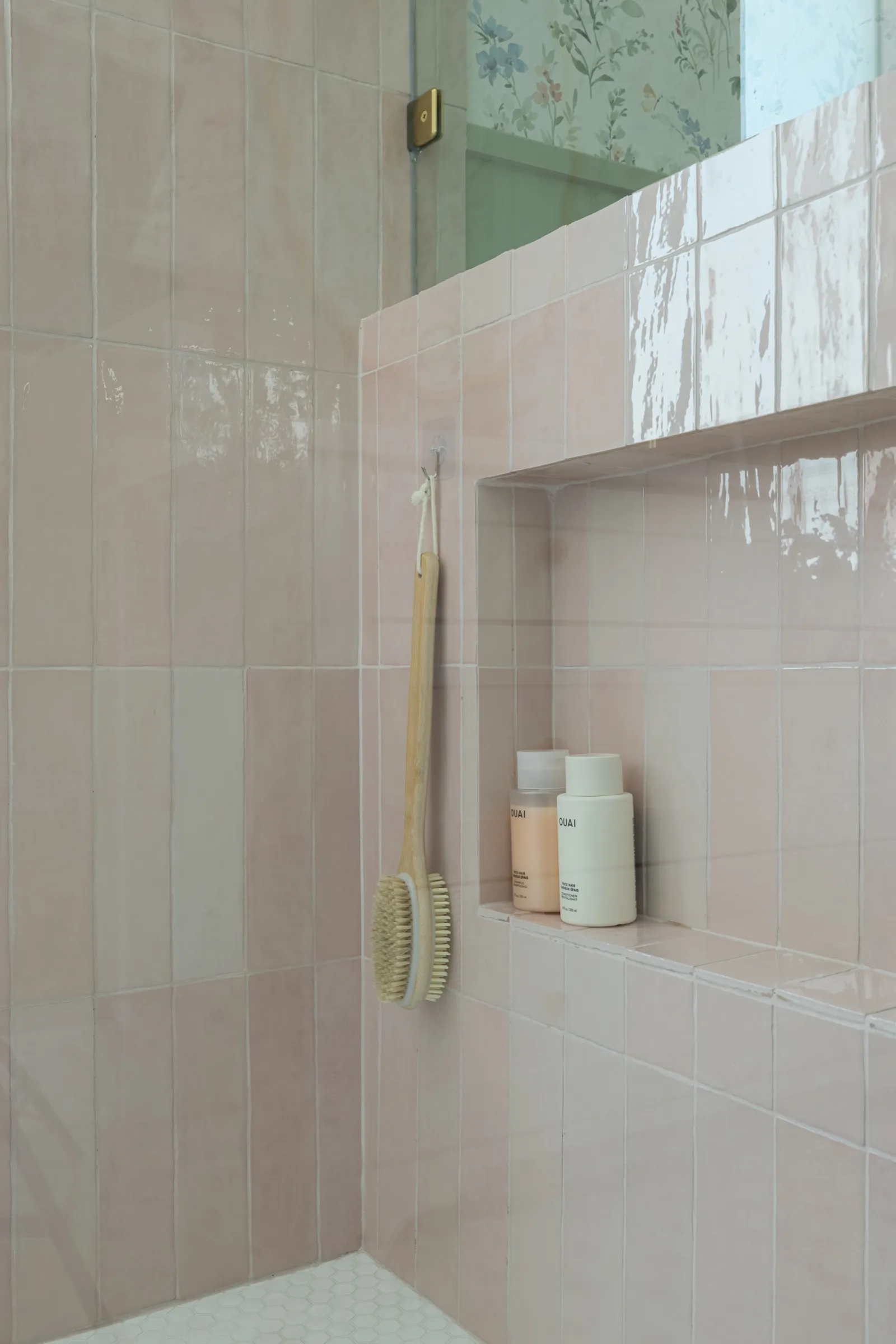Recessed niche in the pink zellige tile holding bottles, with a wooden bath brush hanging alongside