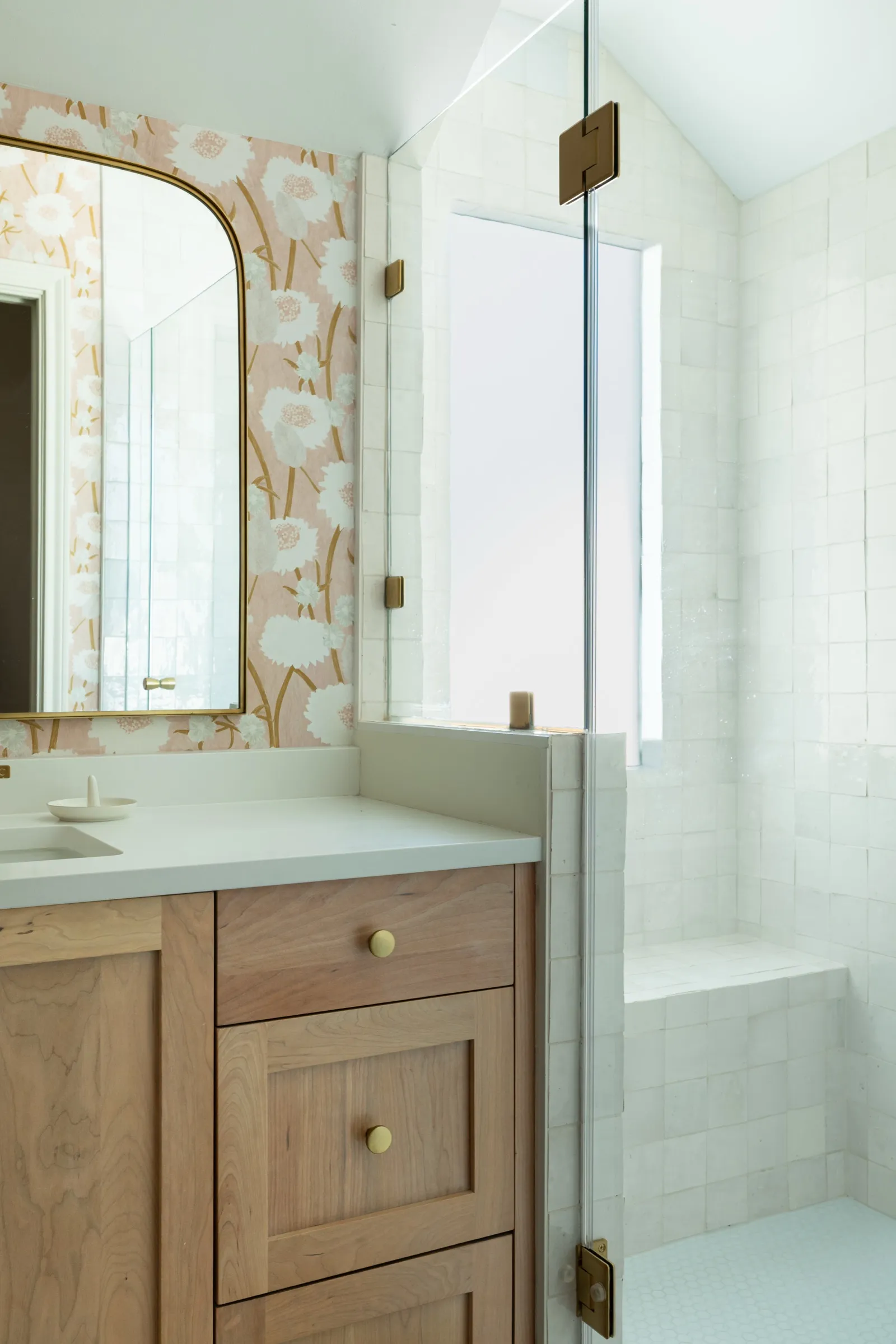 The oak vanity beside the glass shower, white handmade tile catching light from a frosted window