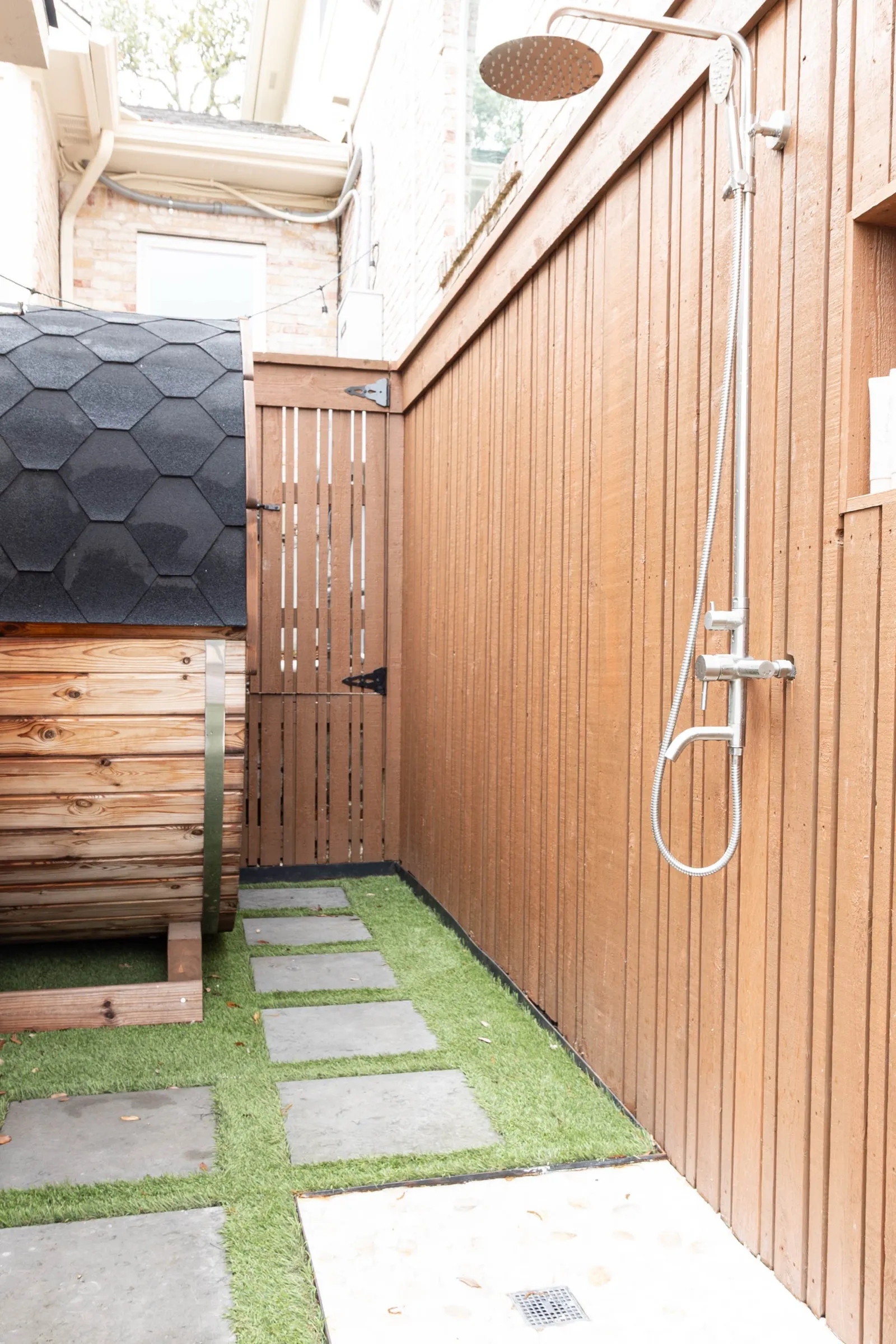 Outdoor shower against the cedar cladding, stepping stones set into turf leading past the covered cold plunge
