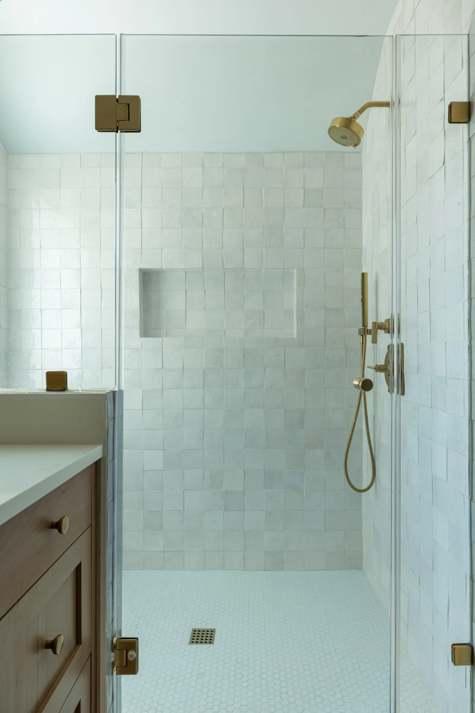 Shower lined floor to ceiling in handmade white tile with a recessed niche and brass fittings