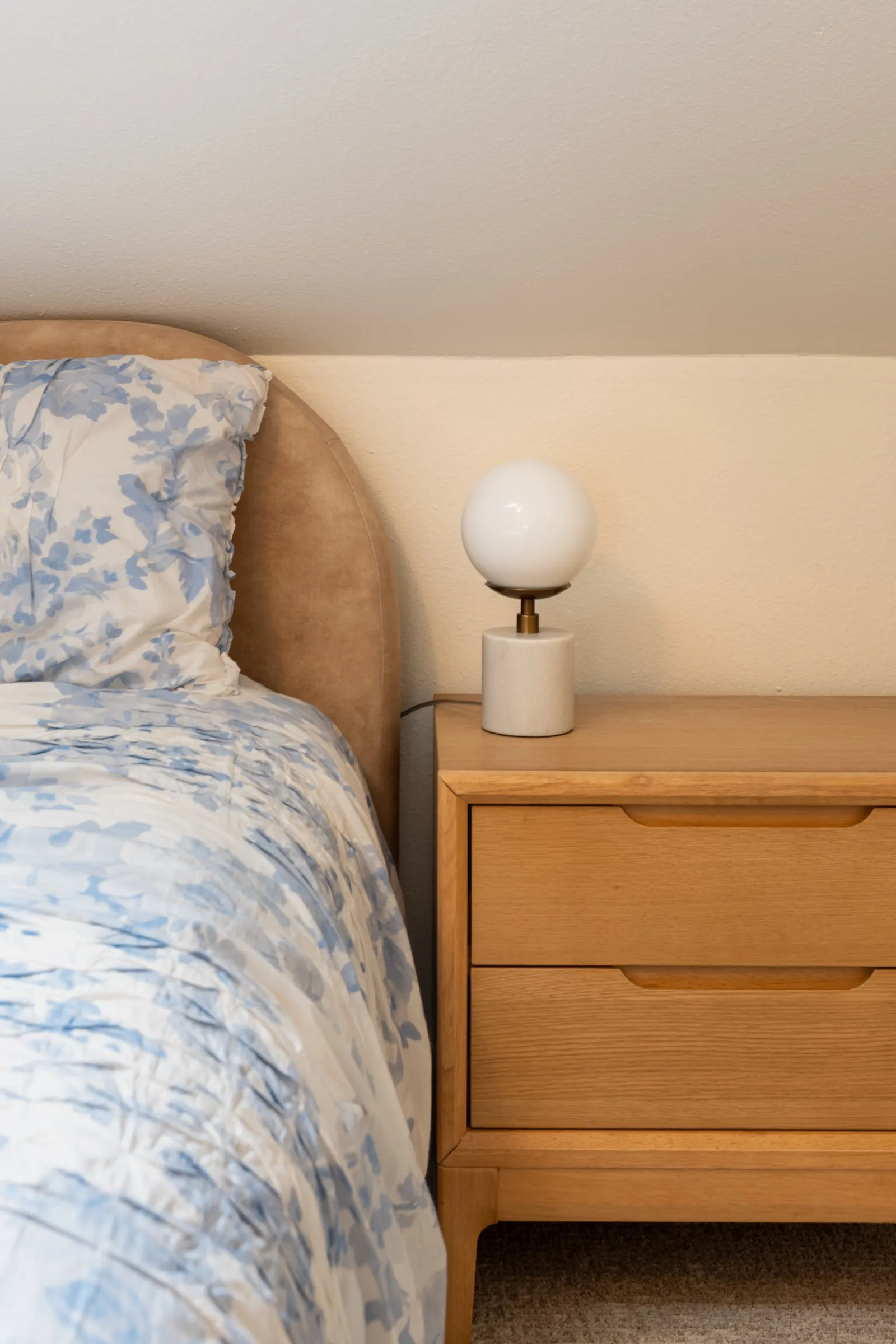 Blue toile bedding against an upholstered headboard, with a globe lamp on an oak nightstand