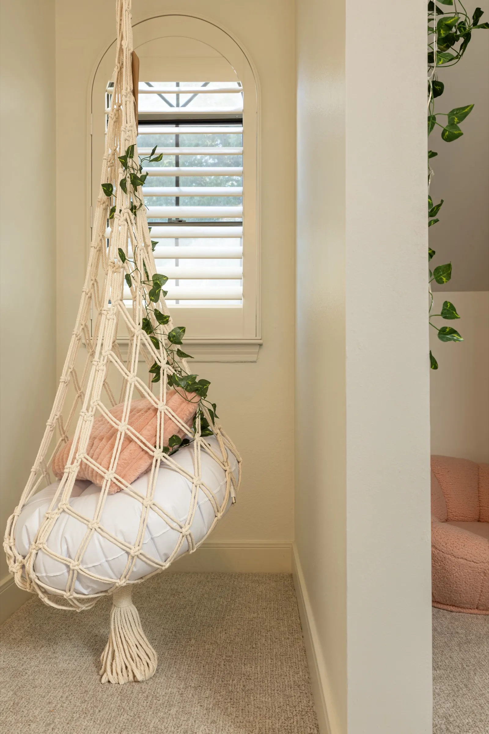 Macrame hanging chair with trailing ivy beside an arched shuttered window