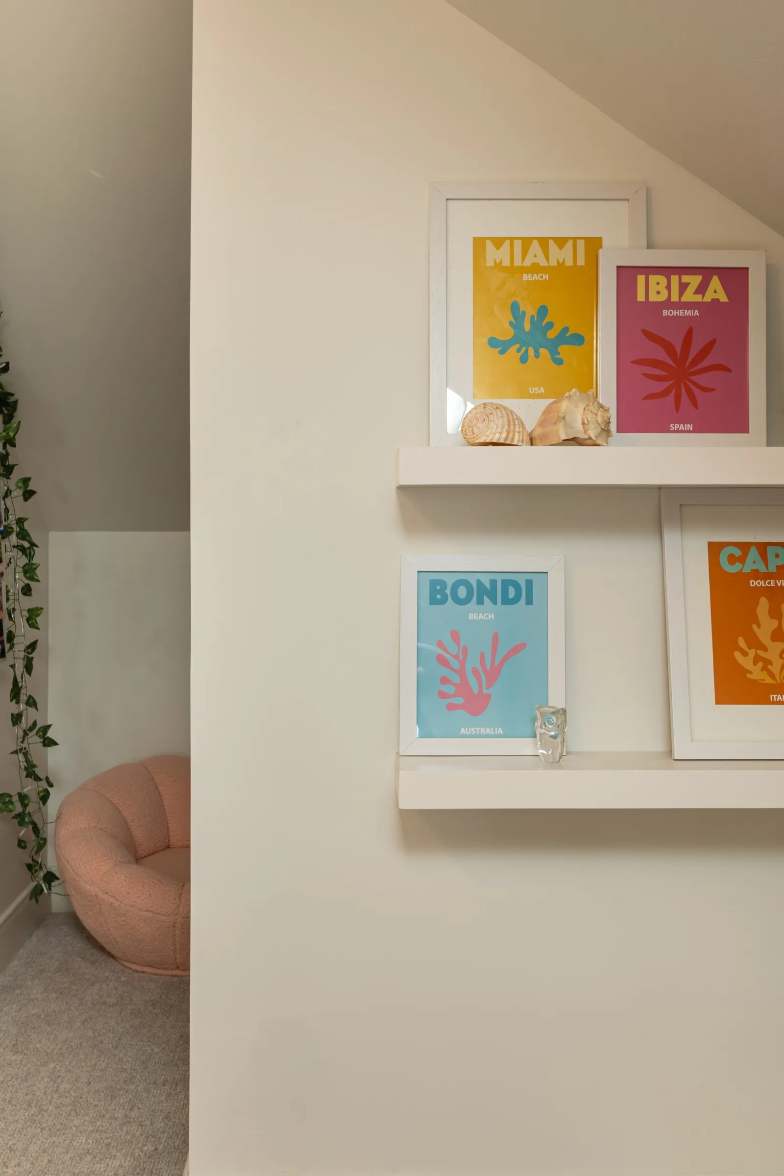 Picture ledges holding bright travel prints, with a pink boucle pouf below