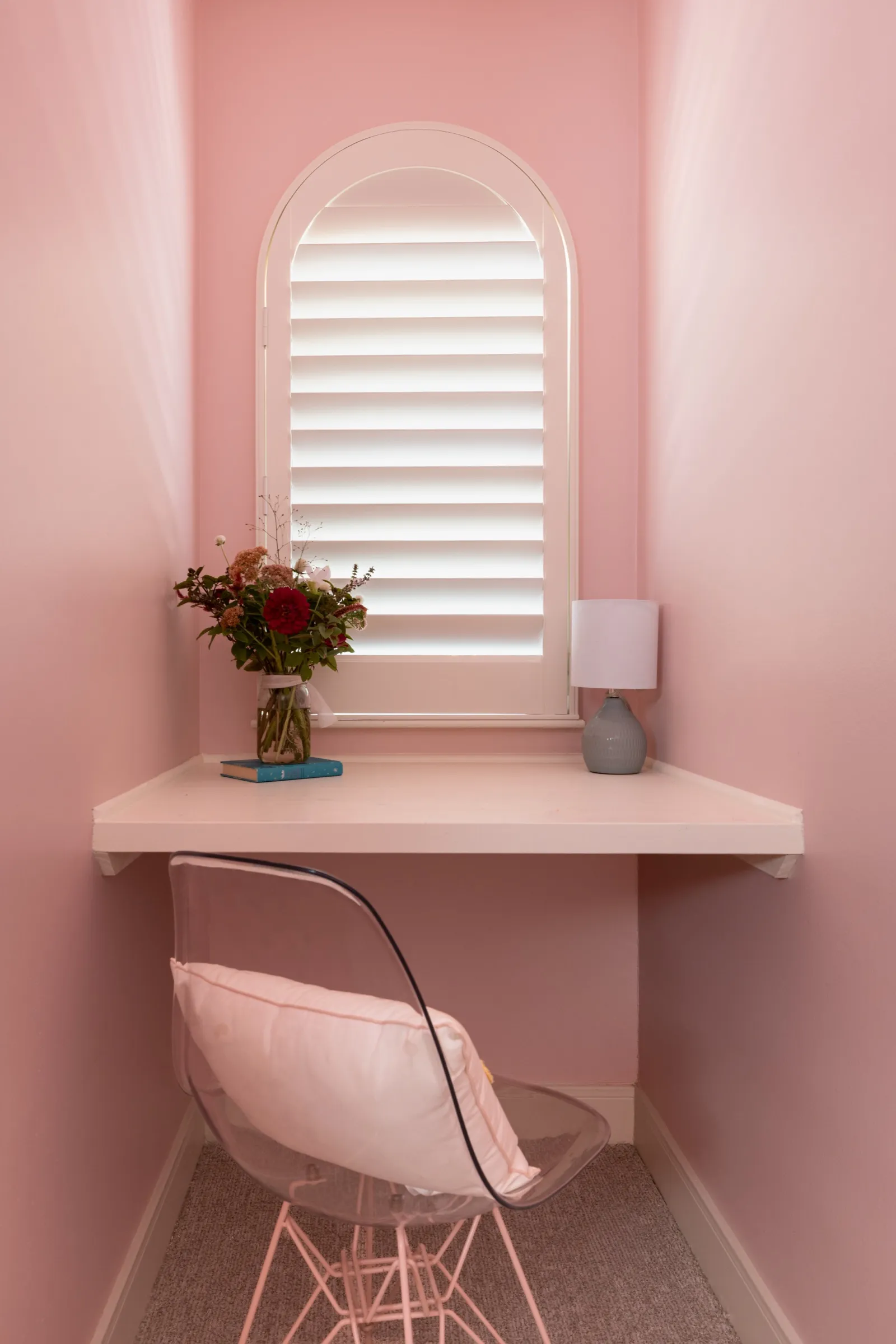 The desk close up: flowers in a glass vase, a small lamp and a pink chair against pink walls